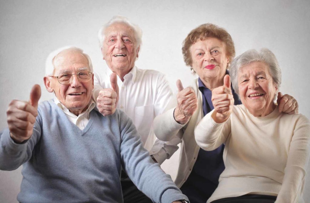 Quattro persone anziane sorridenti col pollice alzato